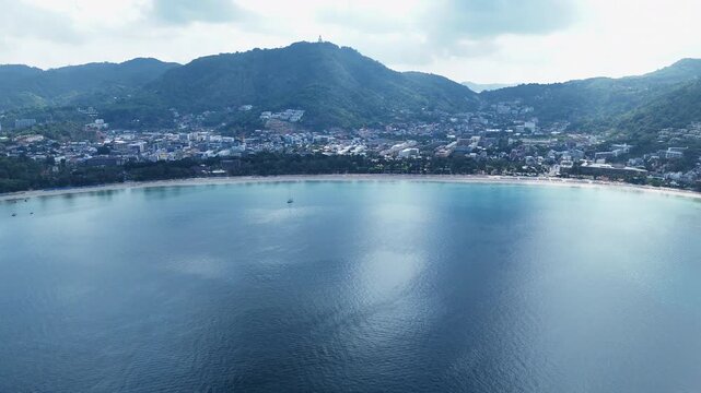 Aerial View of Serene Coastal City and Town with Mountains, Lush Green Hills, and Calm Sea Under Partly Cloudy Sky
