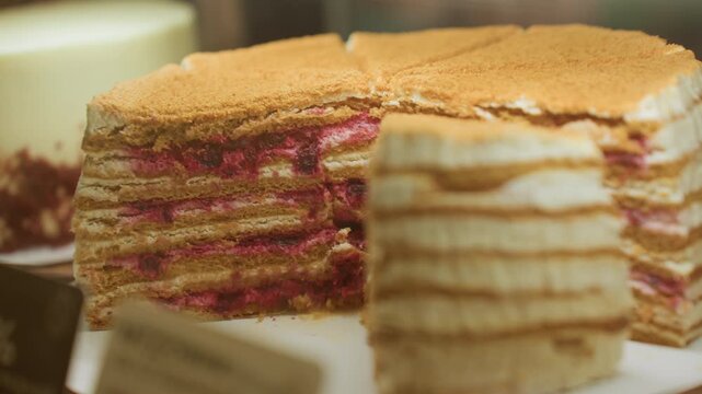Layered cake on cafe counter closeup of multilayer crepe cake with raspberry filling and cream, warm bokeh lighting, glass display case, blurred menu tags, golden crumble topping, artisan bakery
