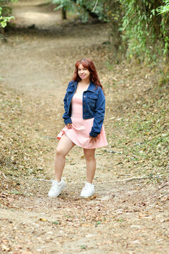Mujer latina de pie en un sendero, vestida con una chaqueta azul y vestido rosado, chica bonita disfrutando de un espacio al aire libre.