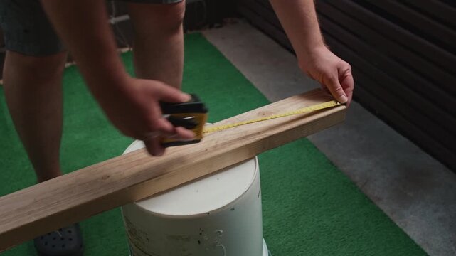 Male hands measuring wooden board with tape measure and marking creating process of precise construction work material preparation and size control during carpentry tasks