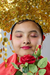 Naklejka premium Young Indonesian Asian Woman Wearing Ornate Gold Traditional Headdress and Red Robe Holding a Red Rose