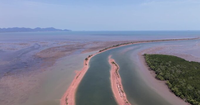 Forward aerial view of a narrow coastal channel flanked by thin reddish sandbanks, leading through mangroves and tidal mudflats in Kampong Samaki with mountains visible on the distant horizon.