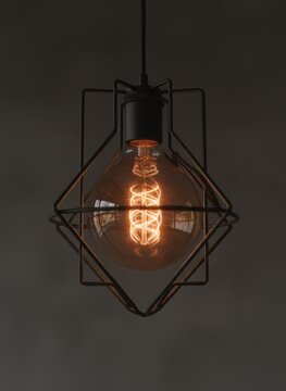 Industrial vintage edison light bulb in geometric black wire cage, decorative glowing filament lamp for interior design, retro hanging pendant light with warm amber glow and metallic frame.