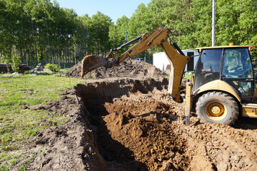 Backhoe excavator digging a deep trench at a construction site, moving soil to prepare ground for...