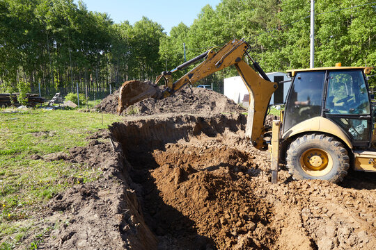 Backhoe excavator digging a deep trench at a construction site, moving soil to prepare ground for foundation
