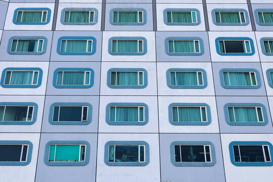 A full-frame architectural shot of a contemporary building's exterior, showcasing rows of blue-tinted windows with a repetitive geometric pattern.