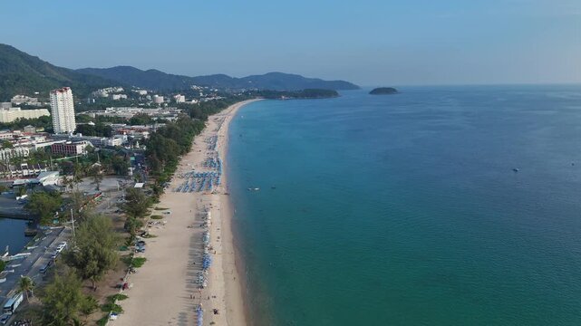 Aerial View of Serene Beach with Clear Blue Ocean, Sandy Shoreline, Distant Hills, and Lush Greenery Under Clear Sky