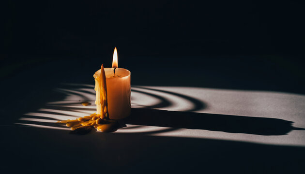 A lit candle with melted wax and shadow on a dark surface.