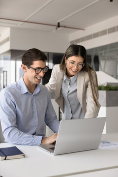 Male female workmates looking at laptop screen with joyful expression, watching amusing content during break in modern coworking office, reviewing sales data, revenue or income growth, feel satisfied