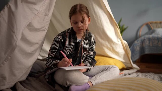 Drawing alone in cozy tent. Young woman writes in peaceful shelter. Female artist attentively creates art inside snug tent with gentle lighting .
