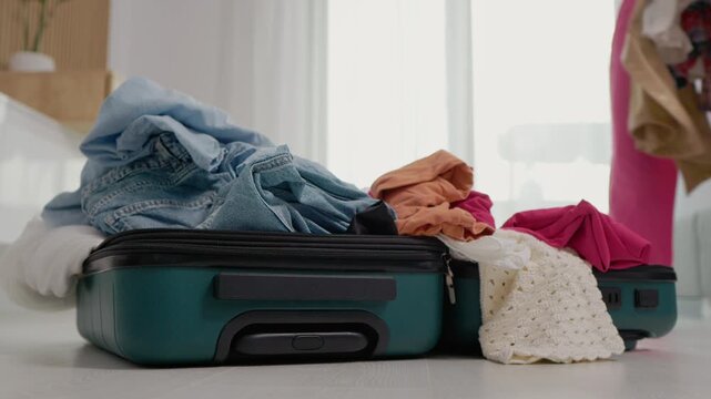 A person tries to fill up a suitcase with more clothes. The suitcase is already full and closing it becomes a challenge. They prepare for a vacation.
