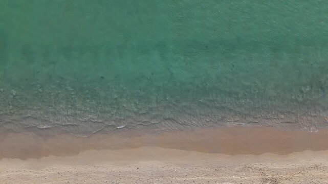 Aerial View of Serene Beach with Gentle Waves Lapping Sandy Shore Showcasing Tranquil Turquoise Sea and Waters