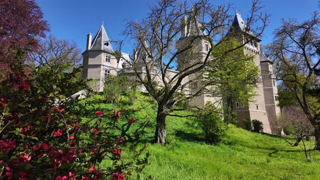 The historic Gołuch&oacute;w Castle with Renaissance architecture and pointed turrets, viewed from the park perspective, surrounded by blooming red flowers and lush green trees under a clear blue sky in brig