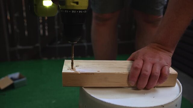 Man making hole in wooden board using electric power tool creating process of material preparation and construction and carpentry tasks