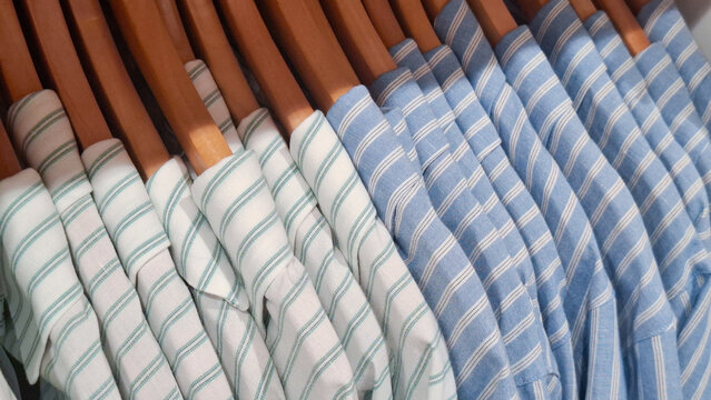High quality striped cotton shirts neatly hanging on wooden hangers in a modern clothing store or home wardrobe organized for lifestyle and fashion retail concept
