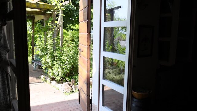Camera slowly pushes into outdoor garden with wooden picnic table and lush green plants through open door on a sunny day.