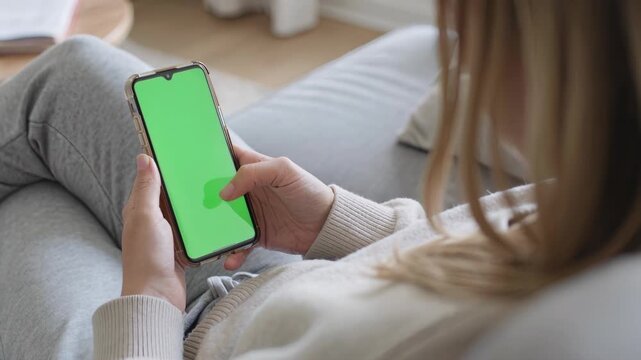 Woman using smartphone with green screen on cozy sofa