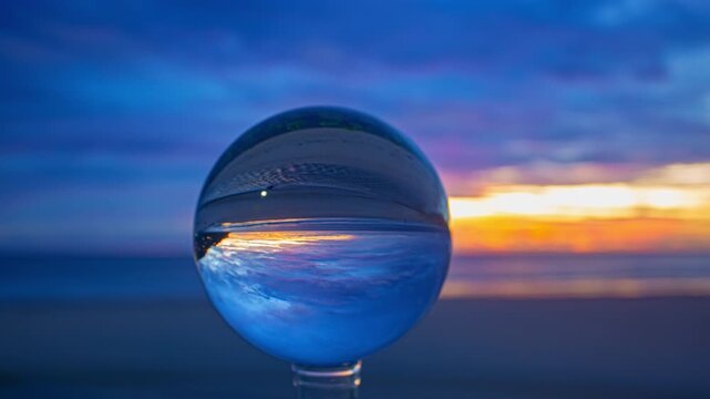 A captivating seaside sunset view enhanced by a glass orb, showcasing refraction and symmetry in nature photography.