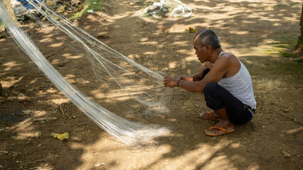 Traditional Indonesian fisherman mending and repairing fishing net in Malang, East Java. © gunungkawi