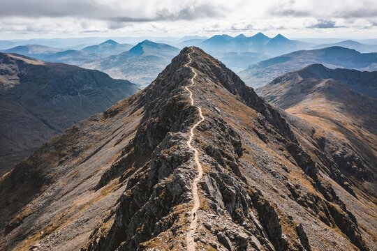 Panoramic mountain ridge with narrow trail leading to pointed summit under daylight capturing exploration and freedom for travel campaigns and outdoor lifestyle branding