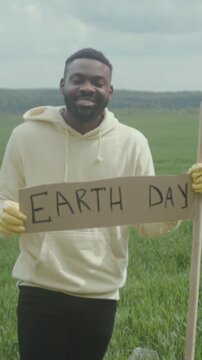 Man with Earth sign outdoors, Dedicated volunteer in peaceful landscape advocates for environmental preservation