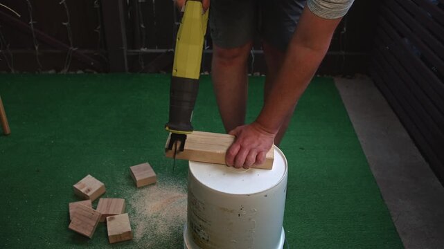 Man cutting wooden beam with reciprocating saw outdoor performing construction work cutting wood into pieces using power tool in outdoor environment