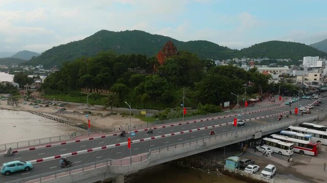 Nha Trang, Vietnam - The Po Nagar Cham Towers, a historic landmark, are seen from a bridge overlooking the city and a river. Traffic flows on the bridge, with buses and cars.
