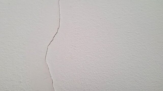 Closeup of a vertical crack running through a light colored painted wall surface, highlighting structural stress or damage and illustrating common household maintenance concerns