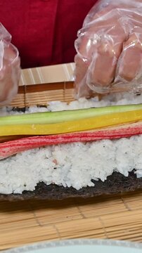 Hands rolling traditional Korean kimbap with multi-grain rice and various ingredients