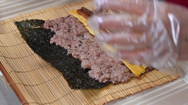 Hands rolling traditional Korean kimbap with multi-grain rice and various ingredients