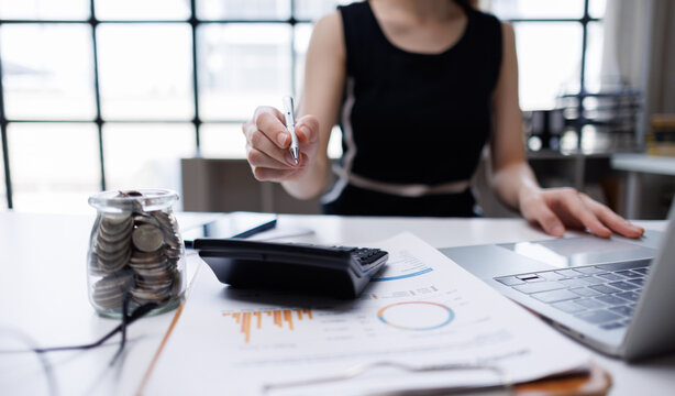 Woman analyzing financial data on laptop with savings jar