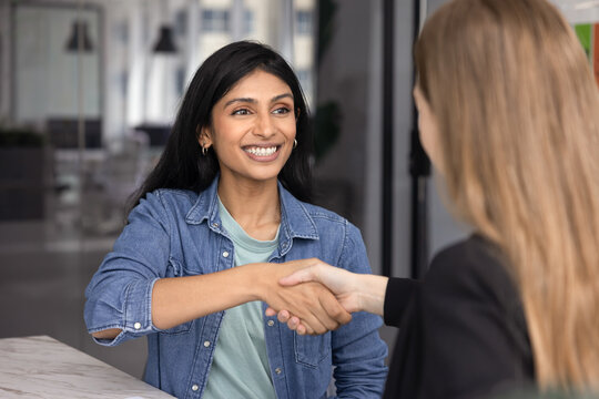 Happy Indian woman shaking hands with female HR manager, start or finalize job interview in company office, smiling, feeling satisfied with recruitment outcome, got job of dream. Headhunting success