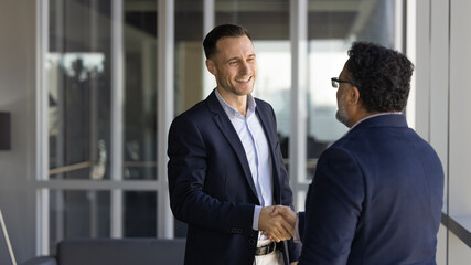 Two businessmen greeting each other with handshake standing in office hallway. Successful collaboration, agreement, client and manager relations, positive business communication and partnership sign © fizkes