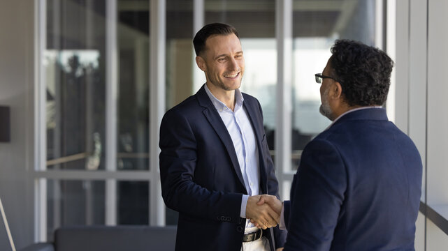 Two businessmen greeting each other with handshake standing in office hallway. Successful collaboration, agreement, client and manager relations, positive business communication and partnership sign