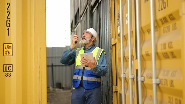 Professional logistics manager in safety gear coordinates shipping operations using a digital tablet and walkie talkie