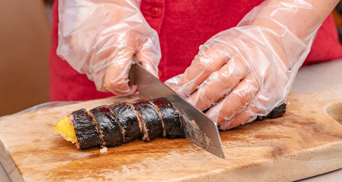 Close up of hands slicing Korean seaweed rice roll kimbap on wooden board