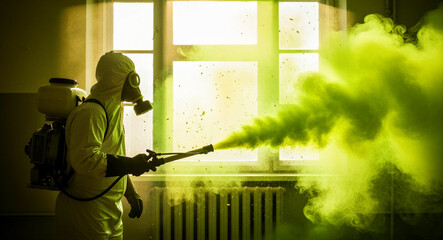 Naklejka premium Person in hazmat suit and gas mask spraying toxic green smoke indoors. Specialist in protective gear performing chemical decontamination. Industrial safety concept for disaster response.