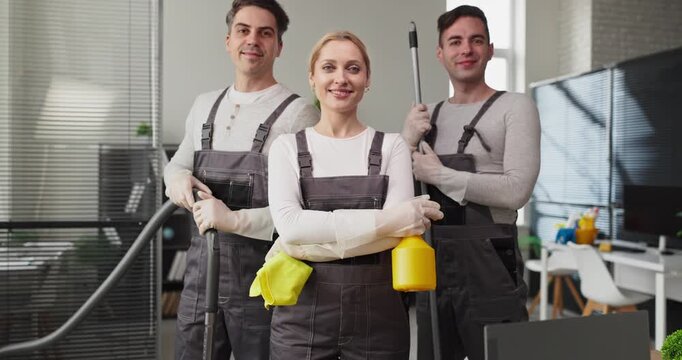 Cleaners team crew janitors provide cleaning service. Three professionals in uniforms with equipment in a bright office, highlighting hygiene. Clear professional cleaning teamwork concept.