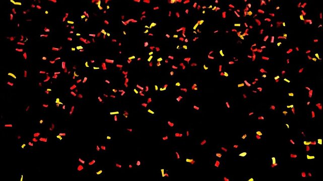 A cascade of vibrant red and gold confetti fills the frame against a stark black background, creating a festive and celebratory atmosphere.