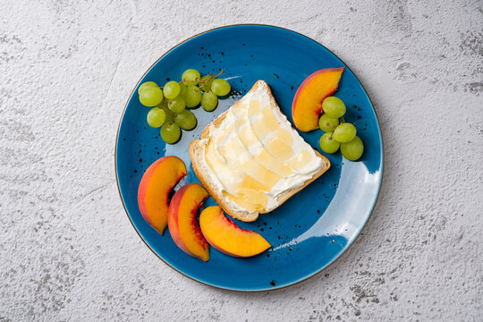 Healthy breakfast plate with toast topped with cream cheese and honey, served with fresh grapes and peach slices