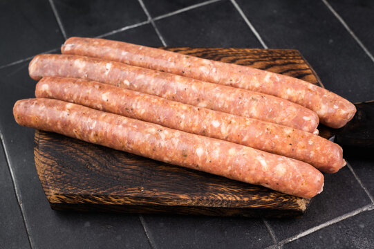 Raw fresh sausages on wooden board over dark slate background. Uncooked pork meat links with spices and fat texture. Butcher ingredient with copy space.