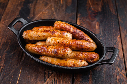 Grilled sausages in cast iron pan with thyme on rustic wooden table. Juicy browned pork meat links ready for dinner or barbecue with copy space.