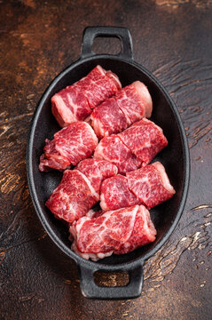 Fresh raw beef chunks for grilling or kebab, marbled meat in cast iron dish with herbs and spices, rustic cooking concept