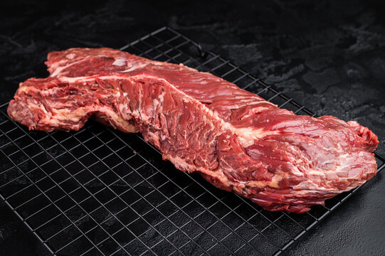 Closeup raw onglet hanger steak on metal grate over black textured surface, rich red meat with visible fibers and fat, ideal for barbecue and cooking