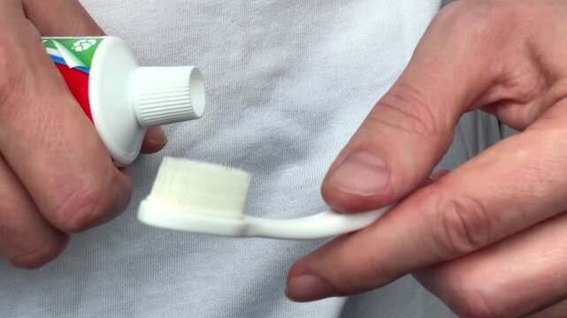 Close up of adult hands holding white toothbrush and toothpaste tube before applying paste for daily dental care