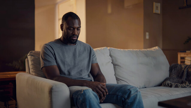 Sad man sitting alone on sofa at home in the evening