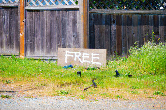 Wooden 'FREE' sign rests on a grassy patch near a wooden fence