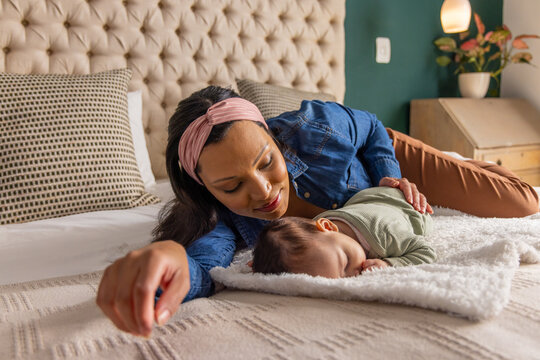 Mother noticing stirring and leaning over sleeping infant, touching back and soothing for comfort