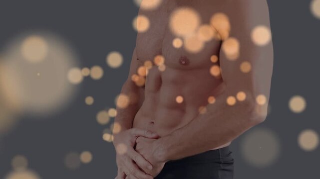 Male model posing in gym, adjusting grip as bokeh appearing and drifting over torso showing muscles