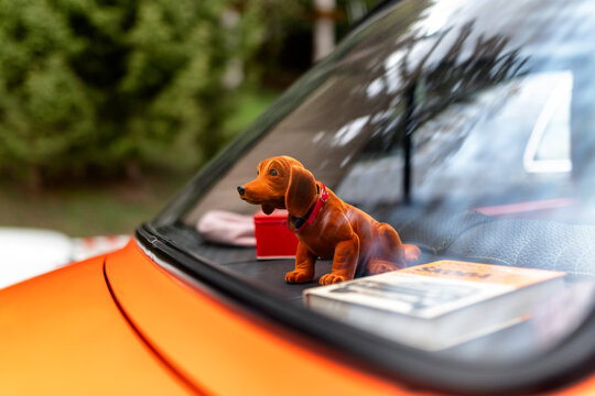 Toy dachshund on rear dashboard of orange vintage car through window